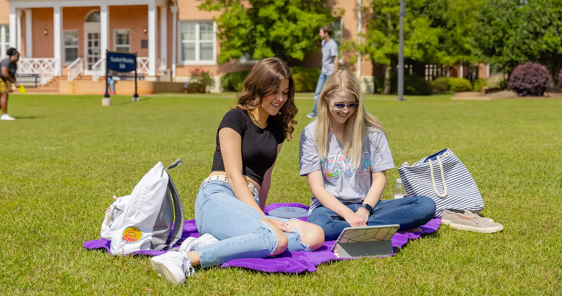 Students sitting on front lawn watching video on tablet
