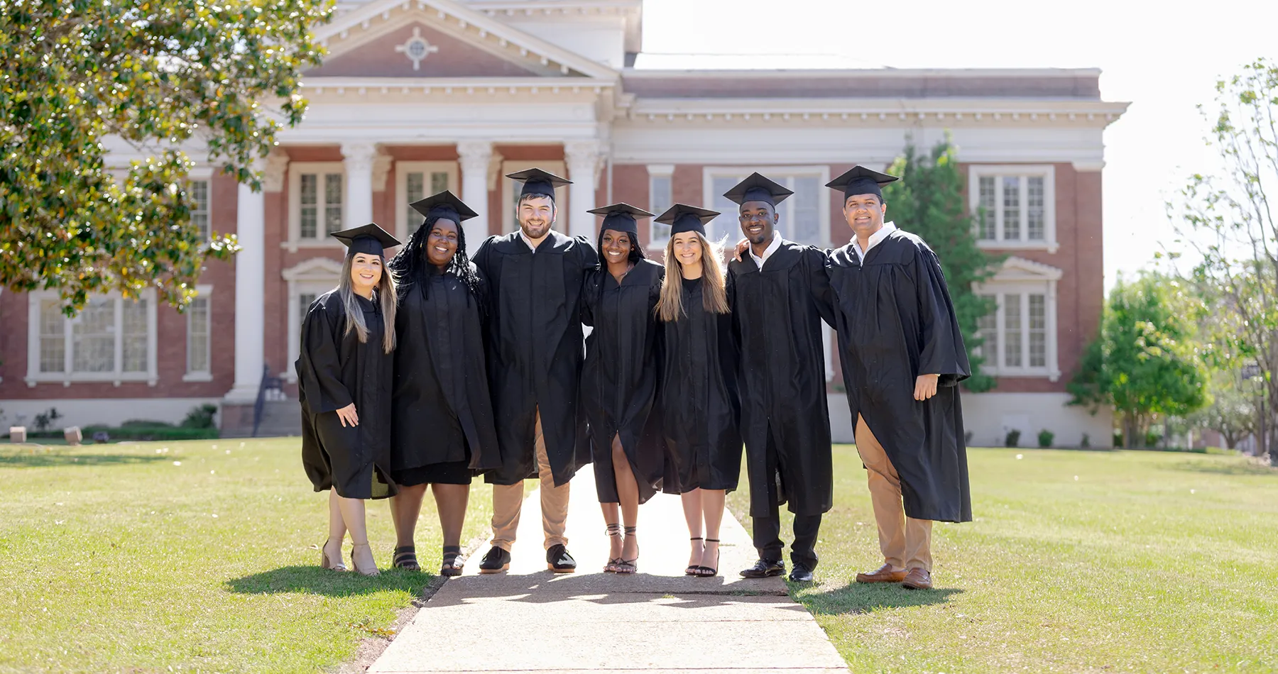 Students in graduation regalia on front lawn
