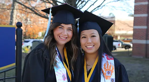 Two graduates of the College of Education in cap and gown
