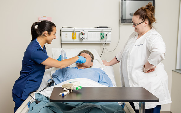 Nursing student receiving assistance from professor with manikin