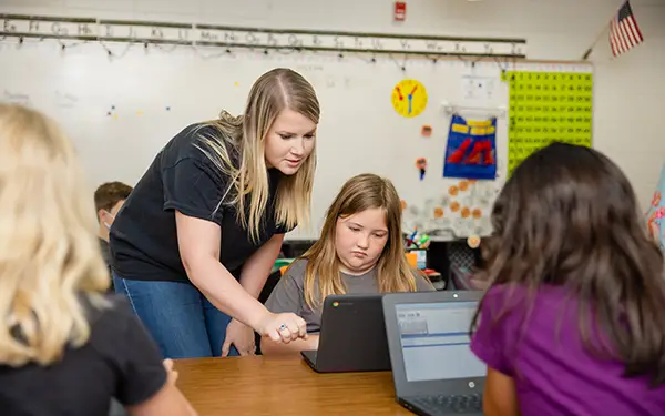 Student teacher assisting elementary student on laptop