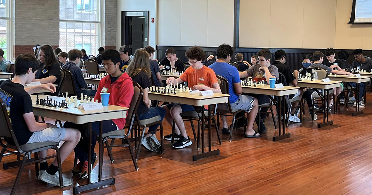 several pairs of students play chess in large room