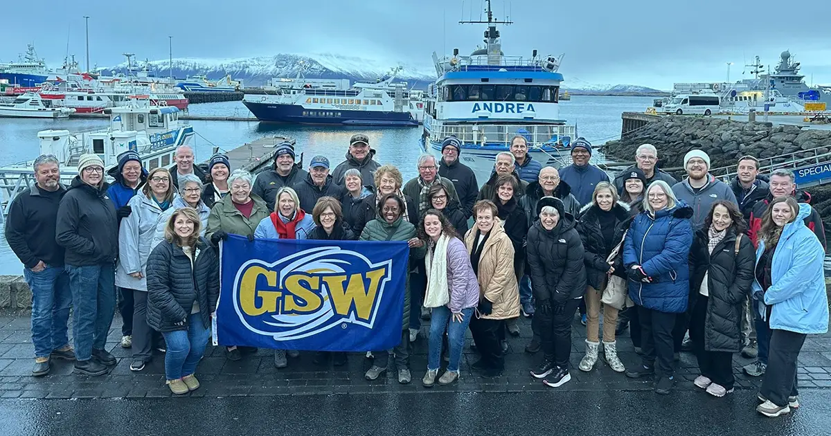 group photo of people holding a GSW flag in front of Icelandic harbor