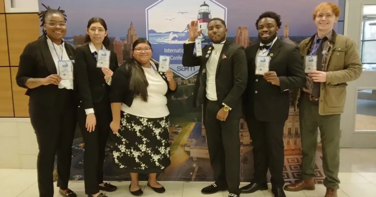 students hold up conference badges in front of backdrop