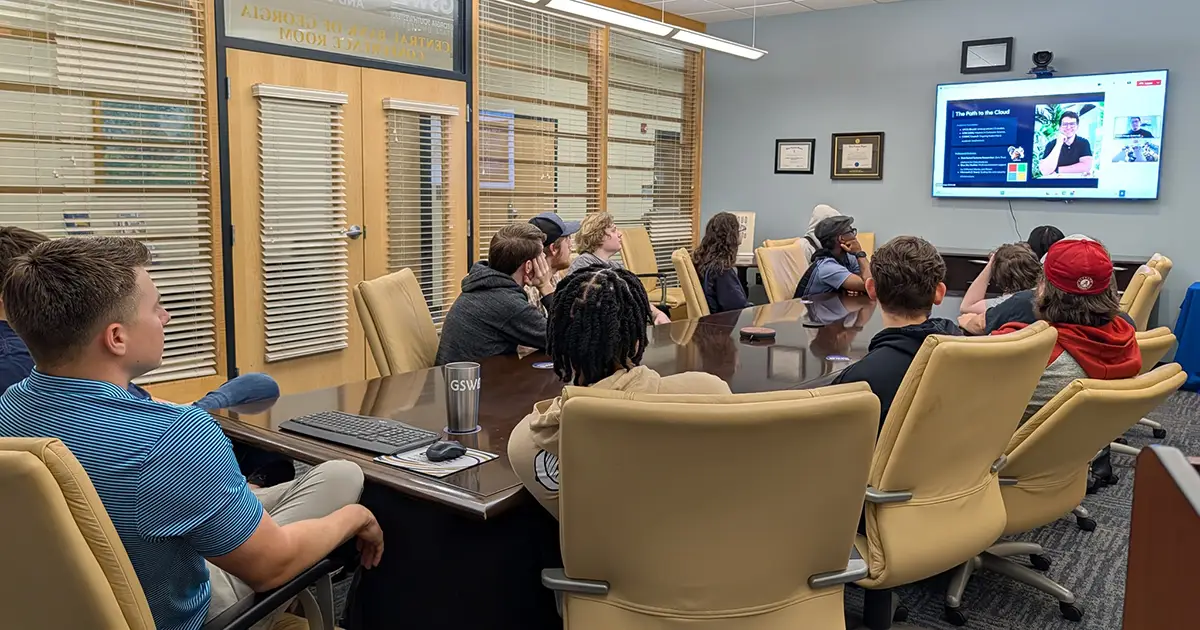 students in conference room face man on a screen