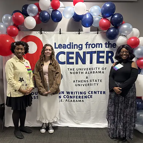 three students pose in front of backdrops and balloons