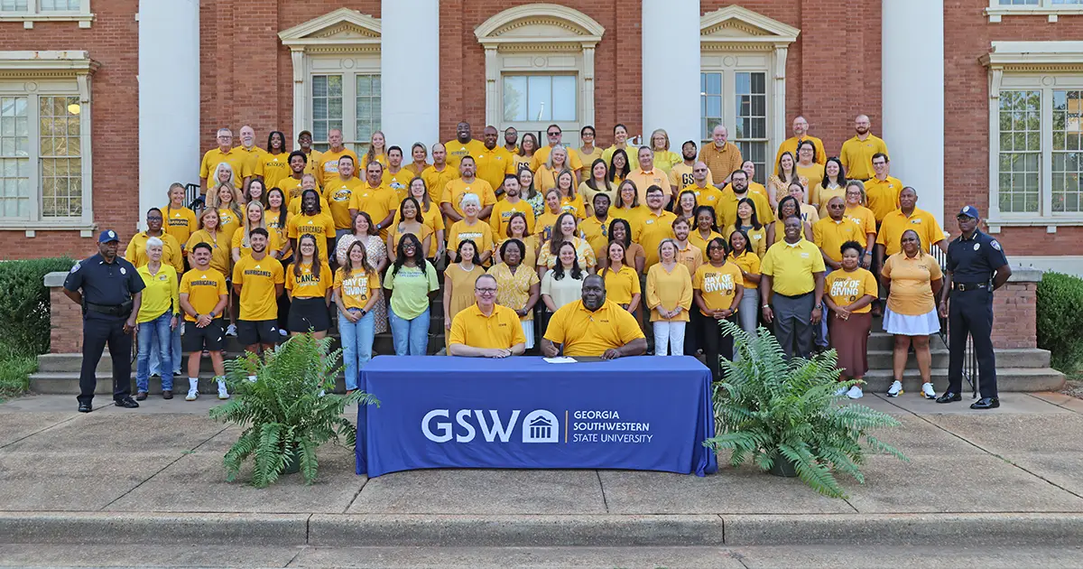 GSW employees stand on front porch of Wheatley Admin building in gold shirts.